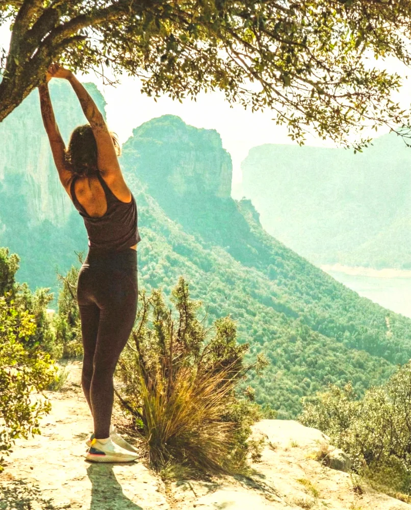 Person practicing yoga in nature overlooking a lush landscape.